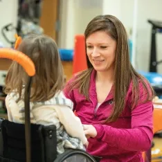 A woman working with a child in a wheelchair to overcome ch所有enges.